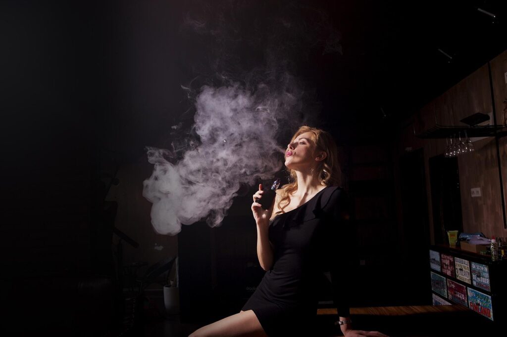 Žena v černých šatech vyfukuje oblak kouře z elektronické cigarety